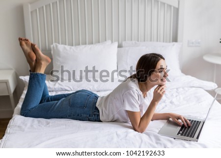 portrait of young woman happy with laptop watching movie at white bed, rejoicing. concept of new technologies, advertising sales and freelance work