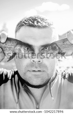 fish eye. outdoor photo of a young handsome man holding two fishes before eyes.
