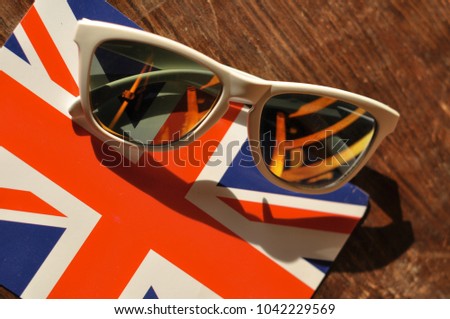white sunglasses laying on the English / United kingdom flag postcard with old vintage wooden table background , summer united kingdom , London touristic destination concept