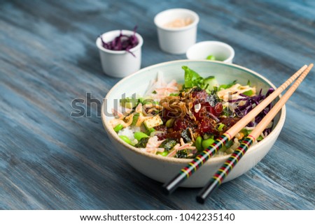 Poke bowl with chopsticks and ingredients. Poke is a traditional Hawaiian dish influenced by japanese and asian cuisine. Ahi poke is made of raw tuna chunks tossed over rice & topped with vegetables.