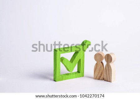 Two wooden human figures stand together next to a green tick in the box. The concept of elections and social technologies. Volunteers, parties, candidates, constituency electorates.