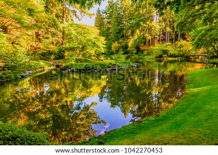 Vancouver BC, Canada
Lake in the park with a mirror image of the sky, trees and shrubs, a wooden footbridge framed by boulders in the autumn sunny day