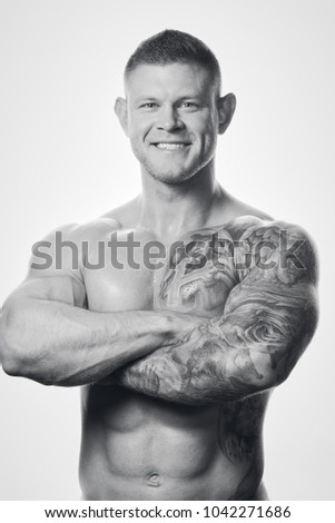 Muscular shirtless man with blue eyes and tattoo smiles on the white background. Black & white