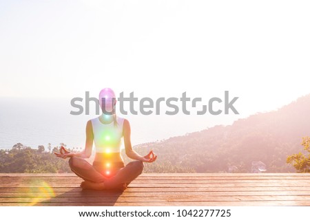 Beautiful woman sits in a pose of a half lotus on high place amazing view of the island outside, she practicing yoga meditation glowing seven all chakra eyes closed calm. Kundalini energy Royalty-Free Stock Photo #1042277725