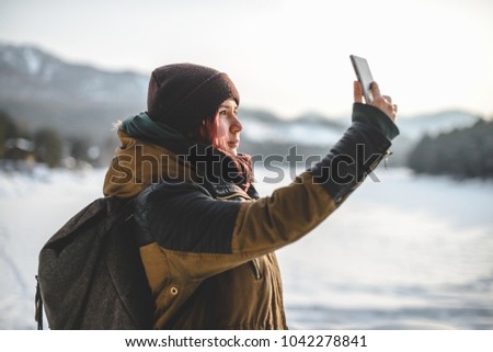 Teenage girl taking a selfie on smartphone, outdoors in winter mountains. 