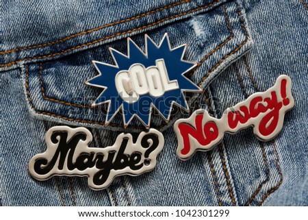 Close up view of denim jacket with cool graphic pins, funky hippie metallic fashion accessories, cool garment brooches