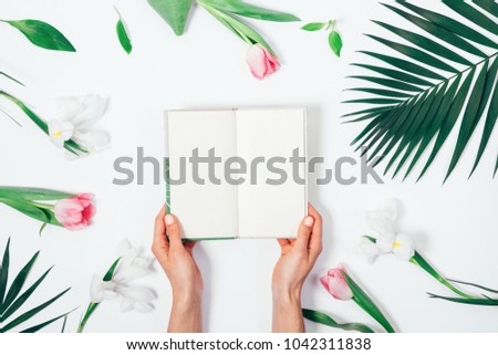Flower arrangement and an open book in female hands on a white table top view