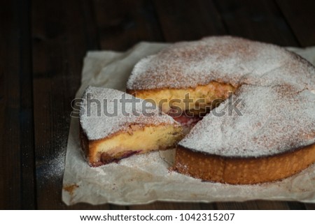 Apple pie with plums with sugar powder on a wooden background