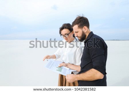 Landscape designer woman come to customer s new house to show sketches, people standing outdoors discussing designs. Fair-haired female in glasses without makeup demonstrating papers to bearded