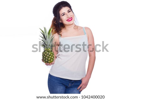 Summer studio portrait of a beautiful young brunette woman with long hair. A girl in a summer T-shirt and jeans is holding a pineapple in her hands. Concept: summer photography and a sunny mood