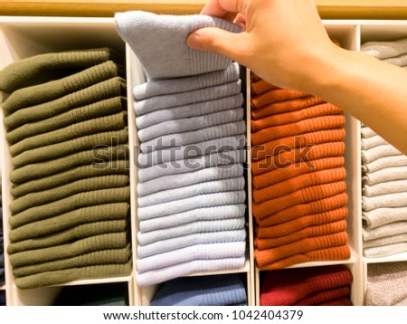 women hand pick the light blue sock from socks stack on shelves for sale in clothing store
