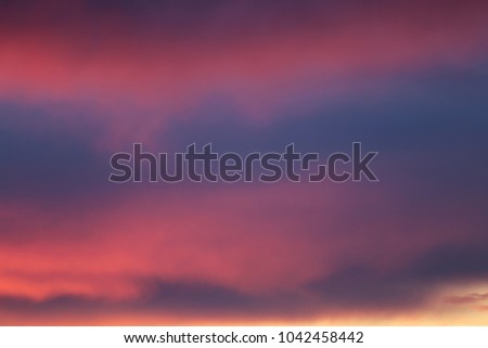 View of a pinky cloudy sky during a sunrise in France. Colorful clouds: pink, blue, orange, purple and grey. Various shapes clouds lighted by the sun. Abstract natural image taken in the morning.