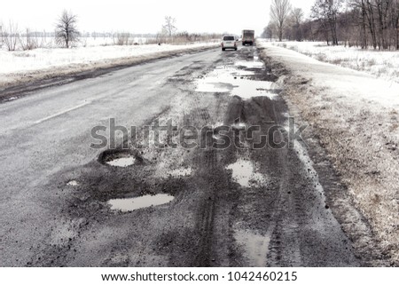 road is paved with cracks in pits and puddles from the snow. Landscape of the winter road in cloudy gray weather. Concept of road repair, opacity for the driver of the car