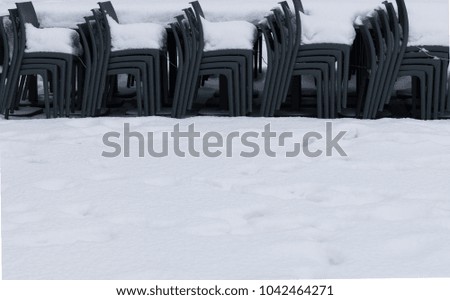 View of piled gray cafe or restaurant chairs covered with snow during winter, off season concept