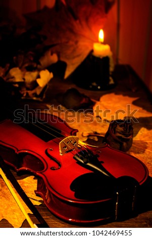 Violin and autumn leaves on the on the table in light of candle in the dark room. Close-up of violin. Focus on the strings.