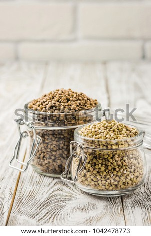 Brown and green buckwheat in glass jars on white wooden background. Selective focus, copy space. 