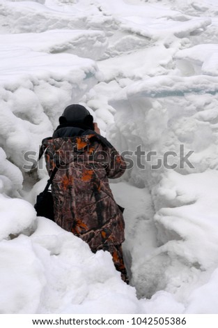Photographer in warm camouflage jacket taking pictures because of snow cracks
