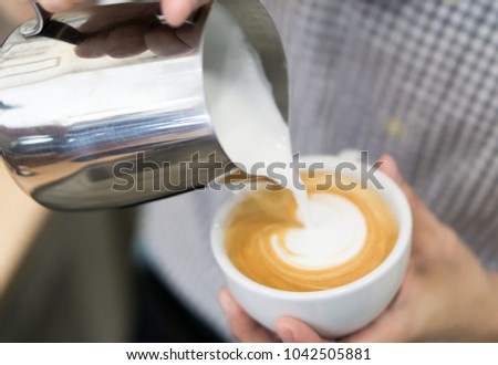 Woman barista pouring stream milk for making latte art coffee with heart shape in white cup, selective and soft focus
