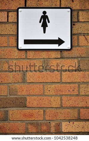 Brick wall with a sign to the women's toilets and an arrow pointing right
