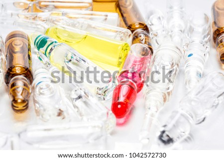 Pile of colorful transparent glass ampoules with liquid medicine isolated on an abstract white background. Healthcare, medical, pharmaceutical and beauty concept. Closeup with soft selective focus