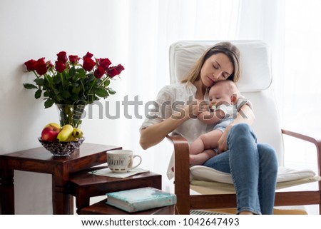 Mother, playing with her toddler boy at home in rocking chair, smiling, breastfeeding