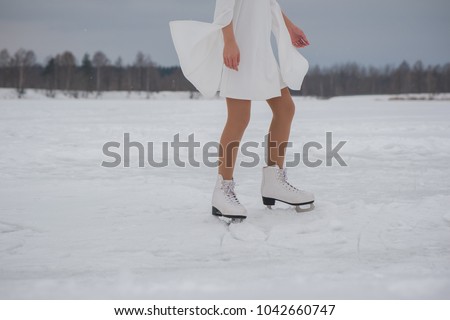 Feet of woman in white dress and skates on snow outdoors at winter