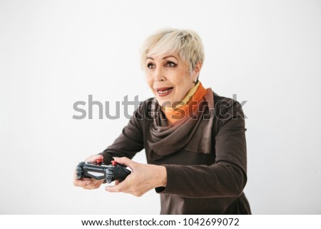 An elderly woman plays a video game and gestures that she won. Elderly person and modern technology.