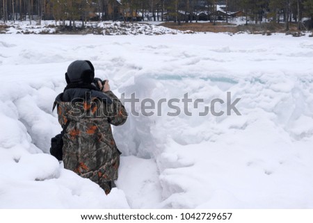photographer in camouflage jacket taking pictures from ambush in winter