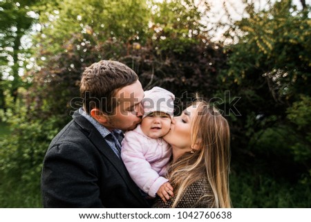 Portrait of mom's dad and daughter in a green park. parents kiss the baby.