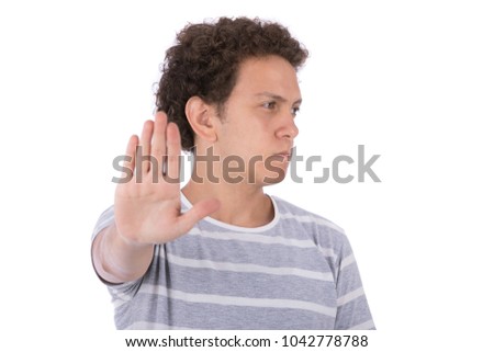 A young man standing and raising his palm as doing the stop sign with a serious face, isolated on a white background.
