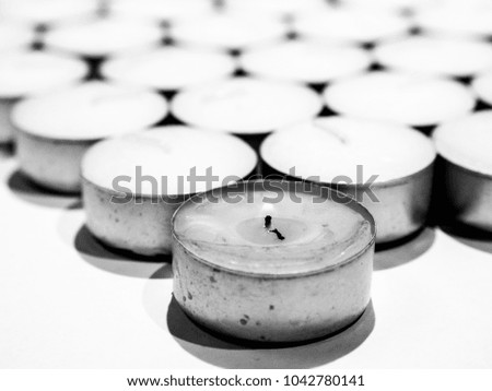 Closeup unsaturated photograph of lots of white tea candles in silver colored metal enclosure organized in rows making a beautiful background image, wallpaper or backdrop.