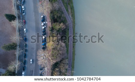Orthogonal aerial view of the Tiber river in Rome. To the side passes the road called Lungotevere. There are trees and cars parked.