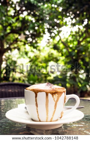 soft focus and blurred of a white cup of hot latte coffee, mess up, with green leaf background texture, overflow on cup, on glass table, vertical
 picture
