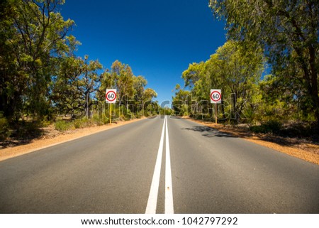 A country road meandering through Margaret River in Western Australia with speed limit signs on either side.
