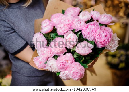 Girl holding in her hands a beautiful bouquet of rose colour peonies decorating with a green leaves
