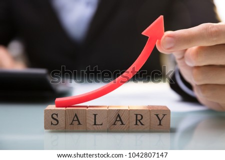Close-up Of A Businessperson's Hand Holding Red Arrow Over Salary Blocks