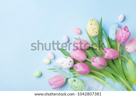 Pink tulip flowers, feathers and colorful eggs on blue table top view. Happy Easter greeting card.