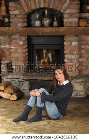 A girl in a blue handmade sweater and socks sitting beside a fireplace