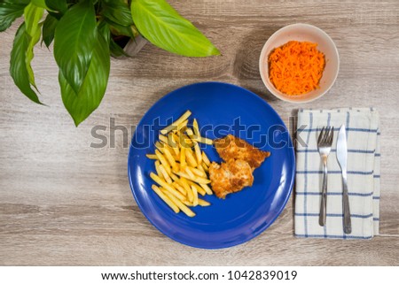 top view of fish and chips and a bowl carrot salad as a side with napkin cutlery pot plant on wooden table