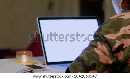 Girl in camouflage clothes works and communicates on Internet. Concept of use gadget protective. Woman looks at white screen laptop. Person talking online