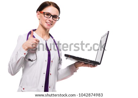 Young beautiful female doctor holding laptop in her hands working on laptop with thumbs up show ok sign on white background