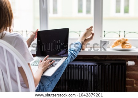 Relaxed Woman working laptop with legs on widnowsill with morning breakfast