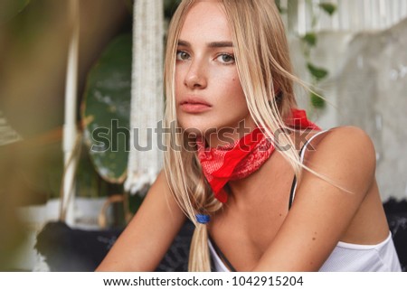 Indoor shot of beautiful blonde woman wears casual clothing looks with serious, confident expression, spends free time in complete silence. Adorable young female thinks or contemplates about something