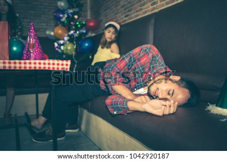 picture of Asian man and woman are very drunk and sleeping on the couch after the end of party. concept of Xmas party, Christmas party and New year party celebration.