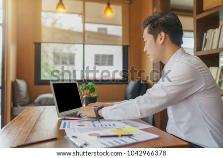 Asianman using laptop computer and financial charts at coffee shop. Male working on laptop in an indoor cafe.