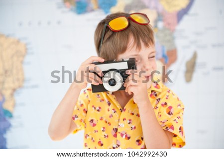 handsome little kid in yellow shirt and sunglasses takes shot with vintage camera on world map background