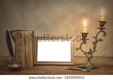 Empty photo frame with copy space, book and burning candle in vintage candlestick and feather pen with inkpot and pocket watch on retro wooden table background. Education. Back to school. Memoirs.