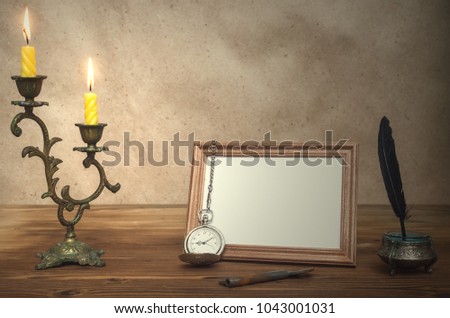 Empty photo frame with copy space burning candle in vintage candlestick and feather pen with inkpot and pocket watch on retro wooden table background. Writer table concept. Education. Memoirs.