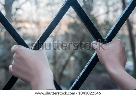 Hands holding on to a metal fence