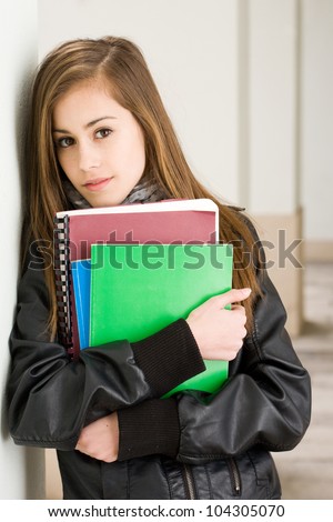 Portrait of a shy young student girl holding colorful exercise books.